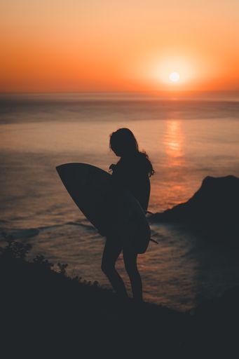 A vertical shot of a silhouette of a woman holding a surfing board