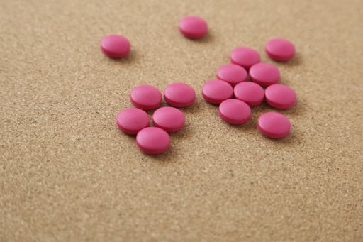 A high angle shot of some pink pills on a wooden surface