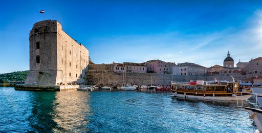 A panoramic view of Dubrovnik's historic city walls and harbor with boats under a clear blue sky.