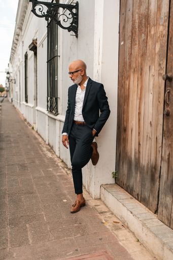 A vertical shot of a professionally dressed middle-aged Hispanic man posing leaning on a wall