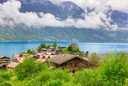 Scenic view of a Swiss village by Lake Brienz with mountains and clouds in the background.