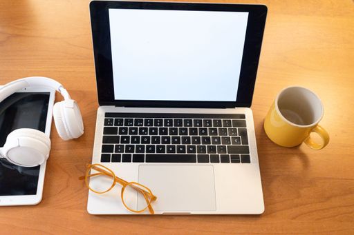 Workspace with a laptop, headphones, glasses, and a yellow mug on a wooden desk.