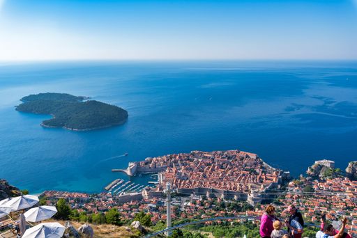 A scenic view of Dubrovnik's old town and the Adriatic Sea from a high vantage point, with tourists enjoying the sunny day.