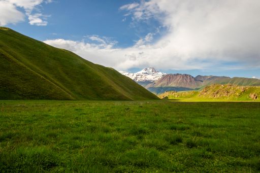 A scenic view of lush green hills and a snow-capped mountain under a partly cloudy sky, showcasing natural beauty and tranquility.