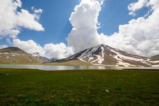 A serene landscape of a snow-capped mountain reflecting in a tranquil lake under a vibrant blue sky with fluffy clouds.