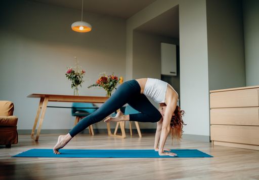 A young female doing Vinyasa yoga on a rug at home