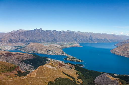 An aerial shot of a lake surrounded by greenery-covered hills and rocky mountains