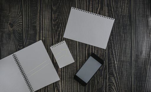 An overhead shot of open notebooks and a phone on a wooden table