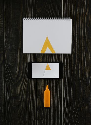 An overhead vertical shot of a marker, phone and painted open notebook on a wooden table