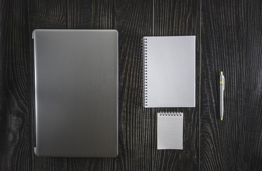 An overhead shot of open notebooks, a pen, and a laptop on a wooden table