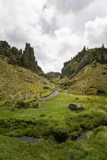 Scenic view of Marcahuasi stone forest with lush greenery and dramatic rock formations under a cloudy sky in Peru.