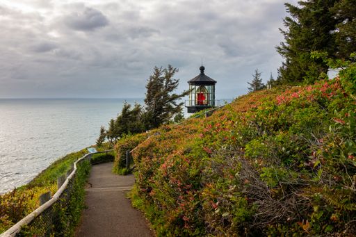 Scenic view of a coastal lighthouse surrounded by lush greenery and a pathway under a cloudy sky.