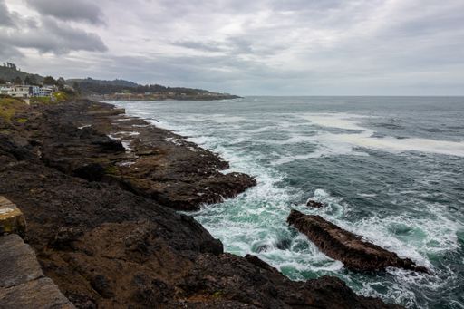 Rocky coastline with waves crashing against the shore under a cloudy sky, showcasing the rugged beauty of the landscape.