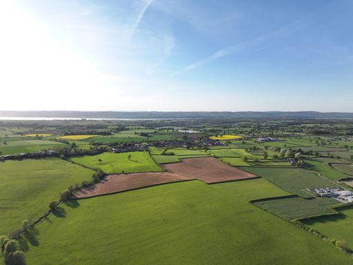 Aerial view of lush green farmland under a clear blue sky, showcasing vibrant fields and distant hills.