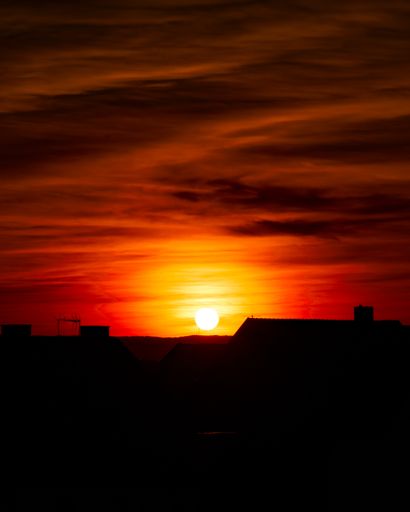 Big bright sun over the building during an orange cloudy sunset, vertical background