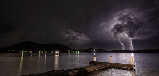 A wooden dock on the sea under a dark cloudy sky during the lightning at night