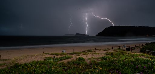 A landscape of a beach surrounded by the sea and hills during the lightning in the evening