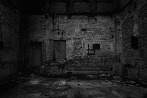 A grayscale view of an old rusty black wall with little shadows with an old broken ground, creepy view