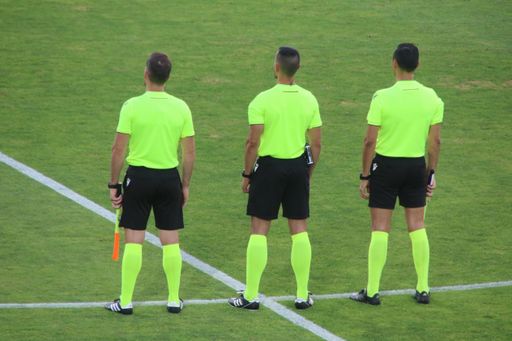 Three soccer referees in bright uniforms stand on a grassy field, ready for the match.