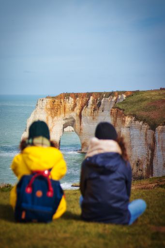 A vertical shot of hikers sitting on the ground and watching the view of Etretat cliffs in France