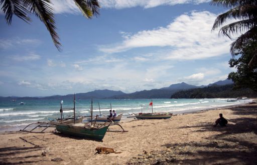 A beautiful view of a small boats on the beach and sitting person in shadow under cloudy sky