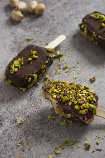 Delicious chocolate-covered ice cream bars topped with crushed pistachios on a textured surface.