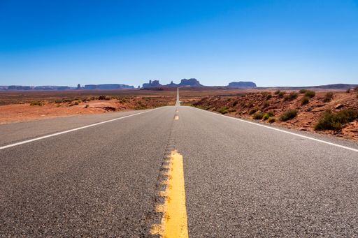 A scenic road leading to Monument Valley under a clear blue sky, showcasing the iconic desert landscape.
