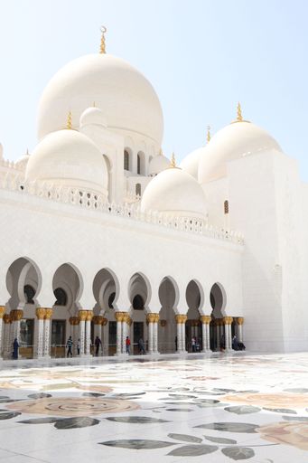 Sheikh Zayed Grand Mosque in Abu Dhabi with intricate floral marble courtyard and people walking, under a clear sky.