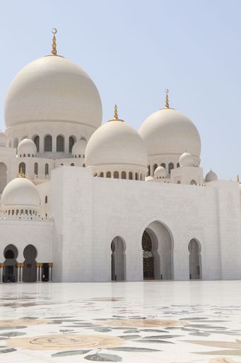 A stunning view of Sheikh Zayed Grand Mosque in Abu Dhabi, showcasing its grand domes and intricate architecture under a clear blue sky.