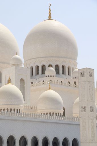 Elegant architecture of Sheikh Zayed Grand Mosque with intricate domes and arches under a clear sky in Abu Dhabi.
