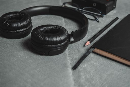 Close-up of black headphones, a pencil, glasses, and a notebook on a gray surface, creating a modern workspace vibe.