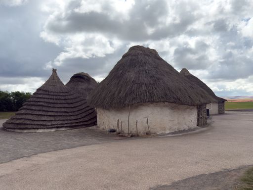 Traditional thatched roundhouses under a cloudy sky, showcasing historical architecture.