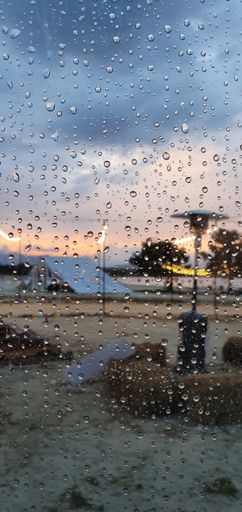 A vertical shot of water droplets on a glass window on the background of a camping site under a pink sky