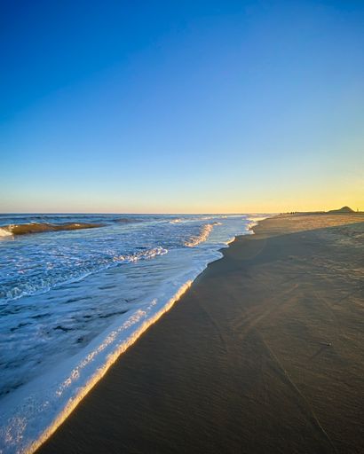 A vertical shot of a foamy seacoast with soft sand under a blue clear sky