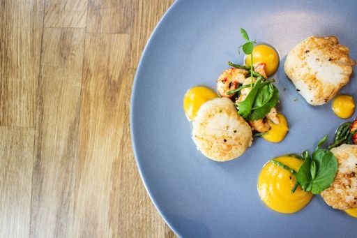 An overhead shot of chicken with shrimps and vegetable leaves on a blue round plate on a wooden surface