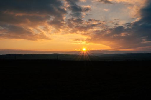 A mesmerizing view of the sunset behind the hills with a field of grass in the foreground