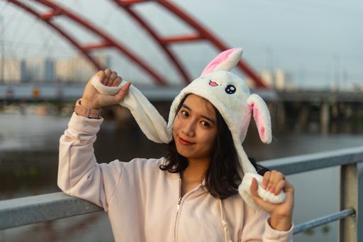 A closeup shot of a smiling Asian female in a cute bunny hat standing on the bridge