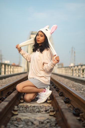 A vertical shot of a young girl with a funny hat on the rail tracks in Saigon, Vietnam