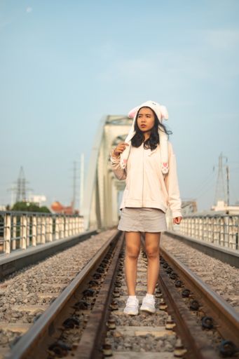 A vertical shot of a young girl with a funny hat standing on the rail tracks in Saigon, Vietnam