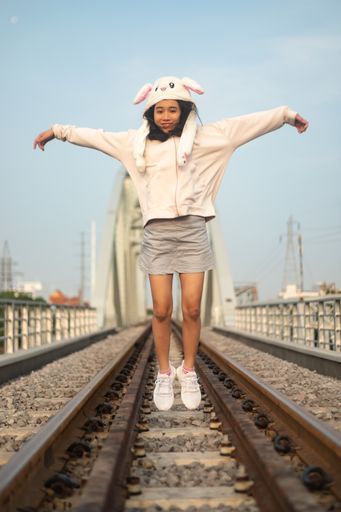 A vertical shot of a cheerful young female with a funny hat jumping on the rail tracks in Saigon, Vietnam