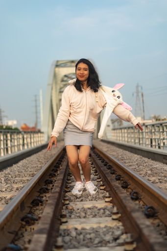 A vertical shot of a cheerful young female with a funny hat jumping on the rail tracks in Saigon, Vietnam