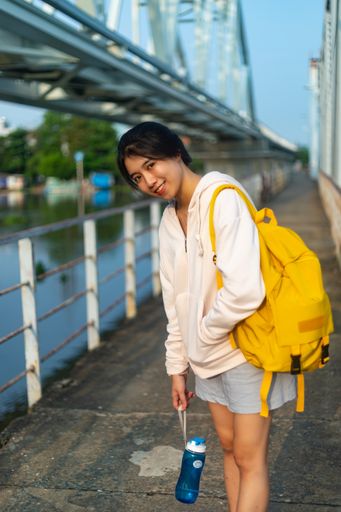 A stylish young female with a yellow backpack standing on a bridge under the sunlight in Saigon, Vietnam