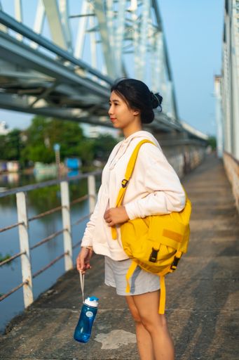A vertical shot of a female wearing a hoodie and a yellow backpack and holding a plastic flask
