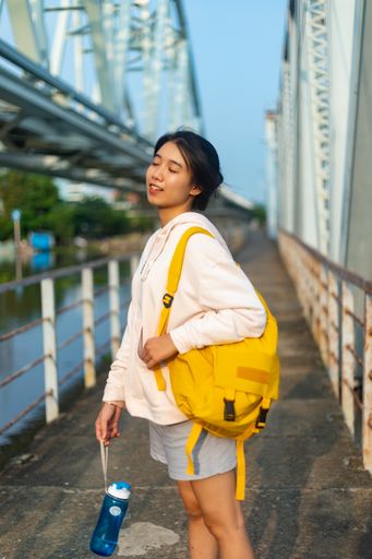 A vertical shot of a female wearing a hoodie and a yellow backpack and holding a plastic flask