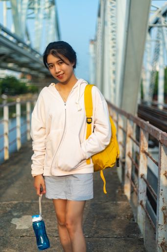 A vertical shot of a female wearing a hoodie and a yellow backpack and holding a plastic flask