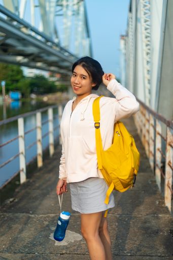 A vertical shot of a female wearing a hoodie and a yellow backpack and holding a plastic flask