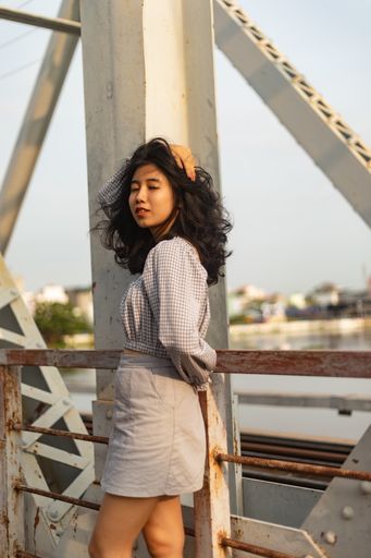 A vertical shot of a female in a nice dress standing on a bridge on a windy day