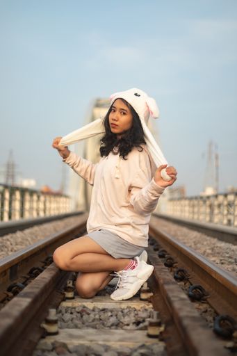 A vertical shot of a female in a hoodie and a bunny hat sitting on the train tracks