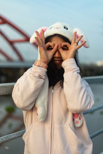 A vertical shot of a female wearing a bunny hat with her hands against her face like glasses