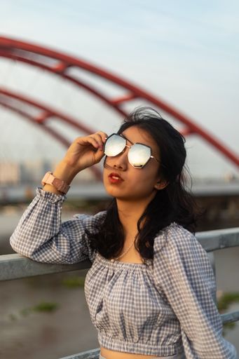 A vertical shot of a female in a nice dress and sunglasses standing on a bridge on a windy day